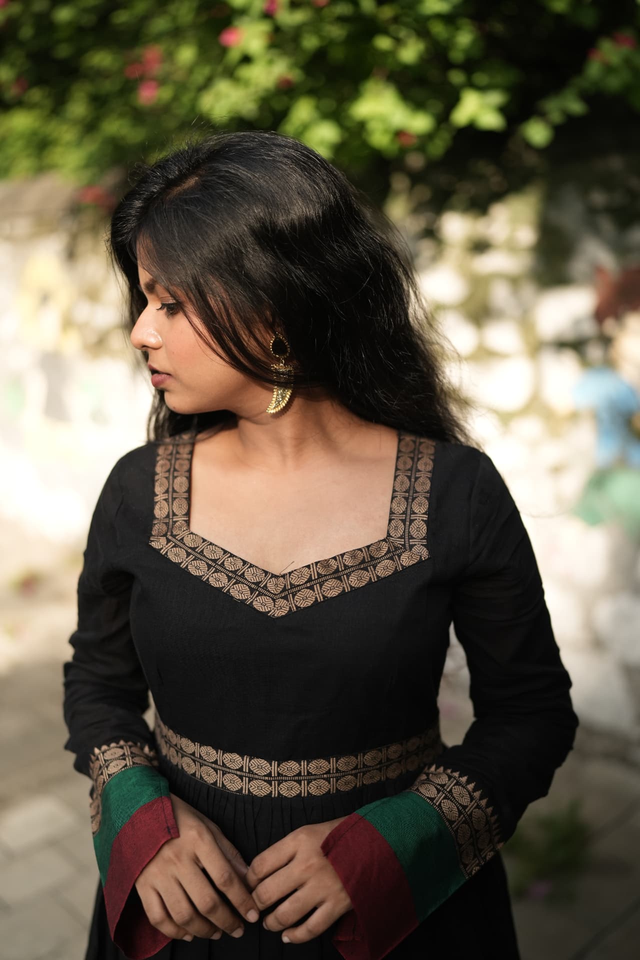 Model in a black long-sleeved kurta with gold zari trim, red and green cuffs, and statement earrings.