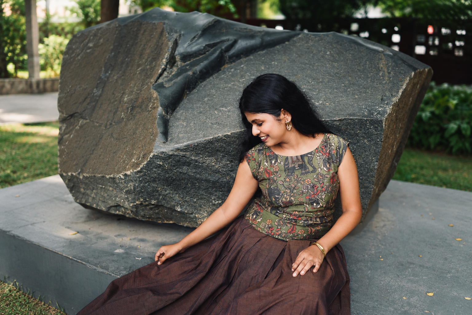 Model in a kalamkari-print top and rust cotton skirt, resting against a stone sculpture in a garden.