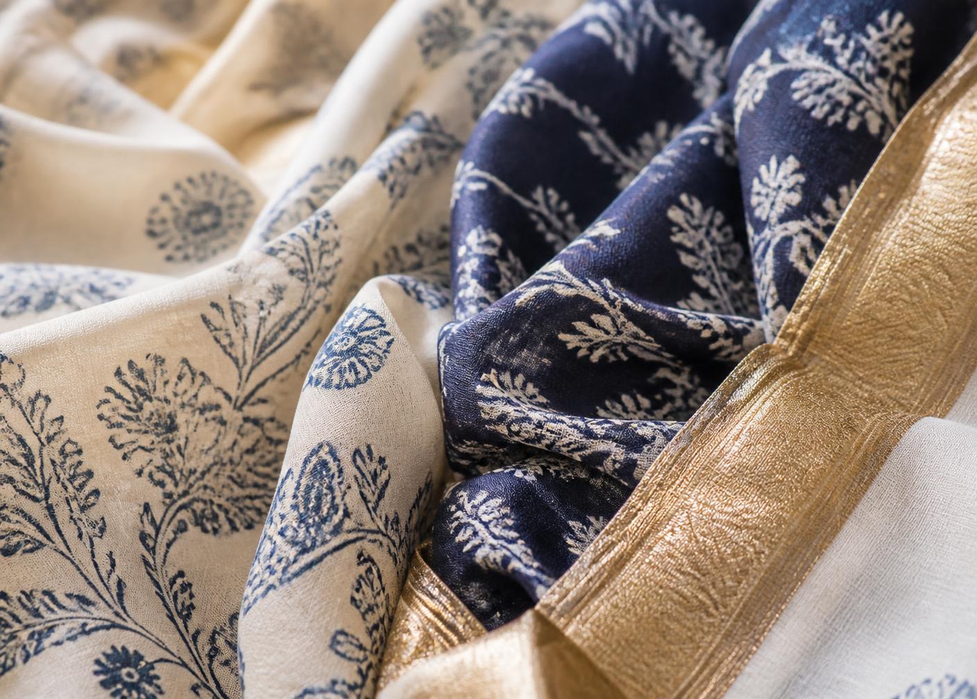 Folds of ivory and indigo hand block-printed Indian cotton and silk beside a woven gold zari border.